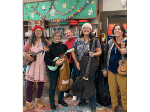 Merry Sunshine band which consists of five musicians holding ukuleles and a bass wearing festive hats in the children's section of the library.