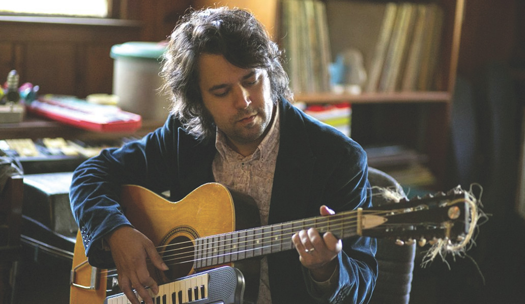 Jay Gonzaelz playing a nylon string guitar with a small keyboard attached.