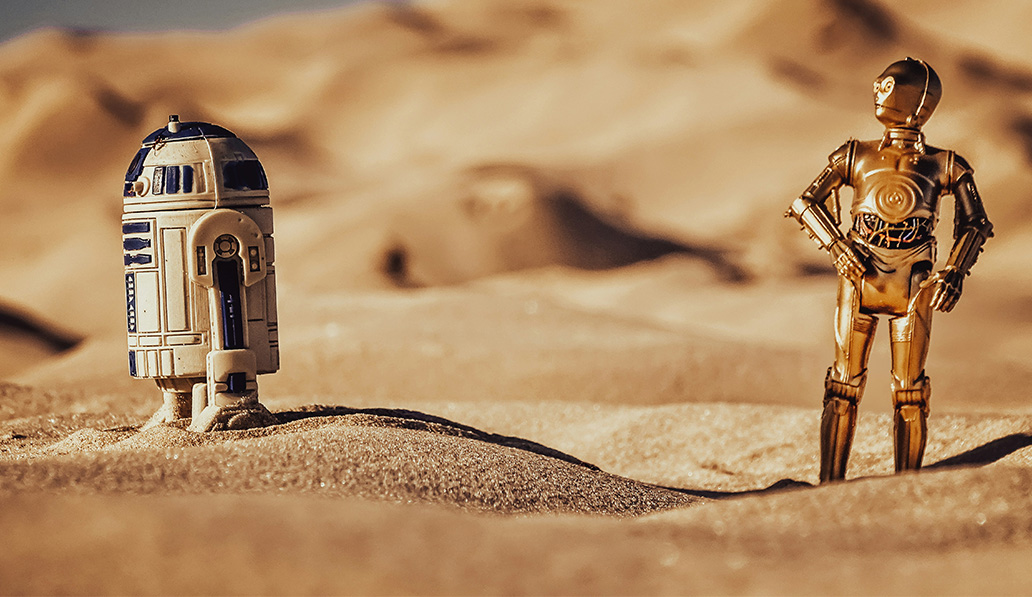 Models of Star Wars characters r2d2 and c3po standing in sand.