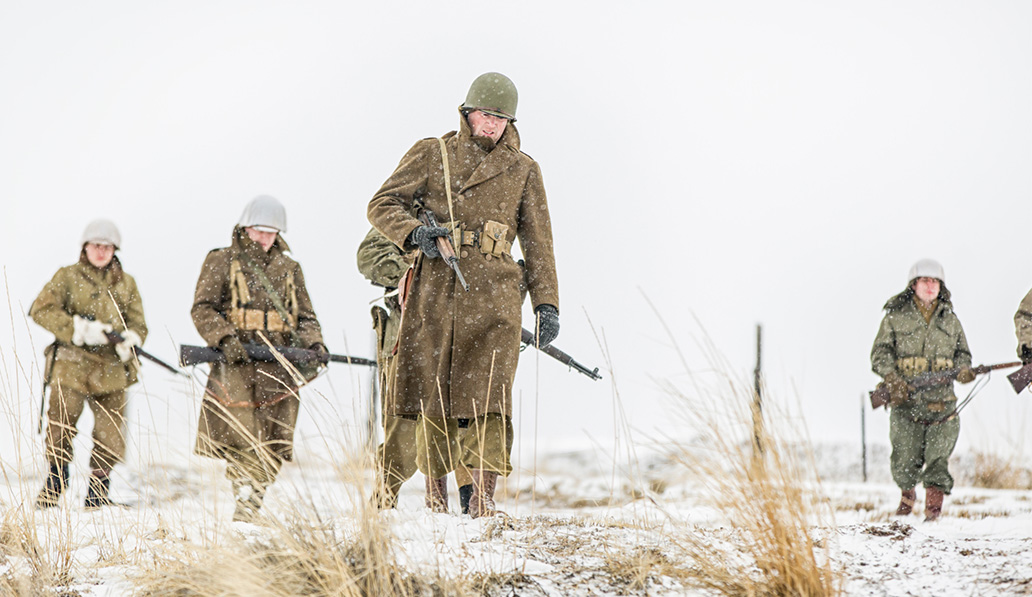 World War 2 U.S. soldier re-enactors walking through snowy field, carrying rifles.